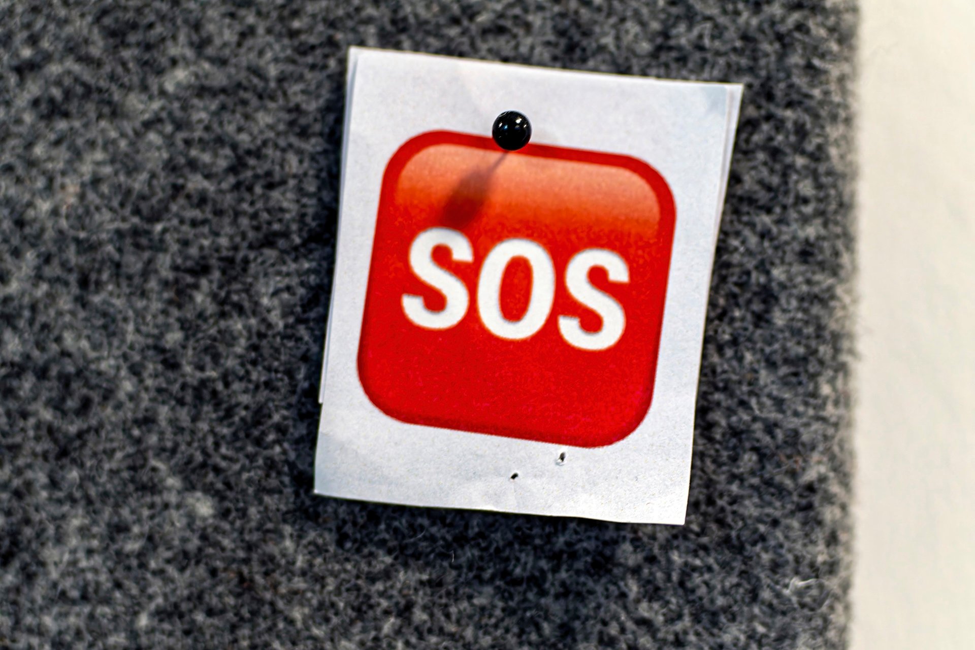 Zettel mit SOS-Aufschrift an einer grauen Pinnwand